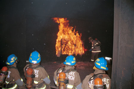 Photograph of four firemen looking at a large fire.