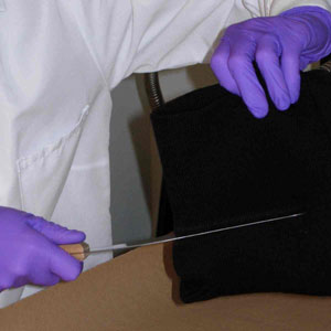 A photograph showing an examiner processing a ski mask using the scraping technique
