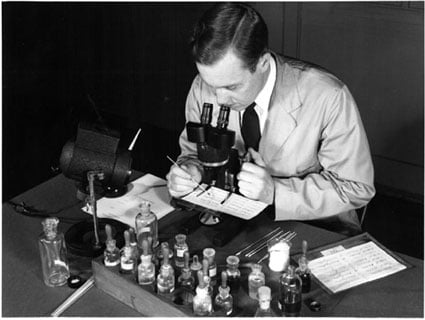 A historical photo of a Laboratory technician examining ink on questioned documents